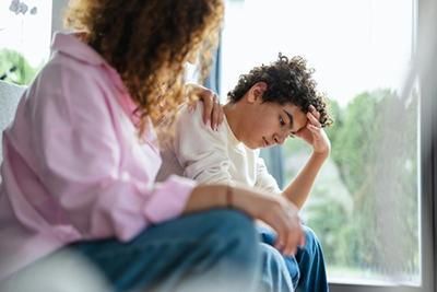 A woman is comforting a young boy who is sitting on a couch.