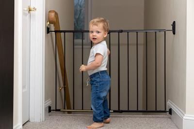 A toddler is standing in front of a baby gate in a hallway.