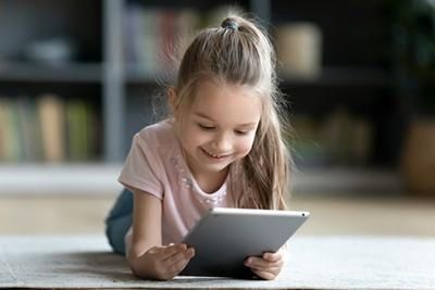 A little girl is laying on the floor using a tablet computer.