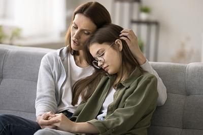 A mother is comforting her daughter who is sitting on a couch.