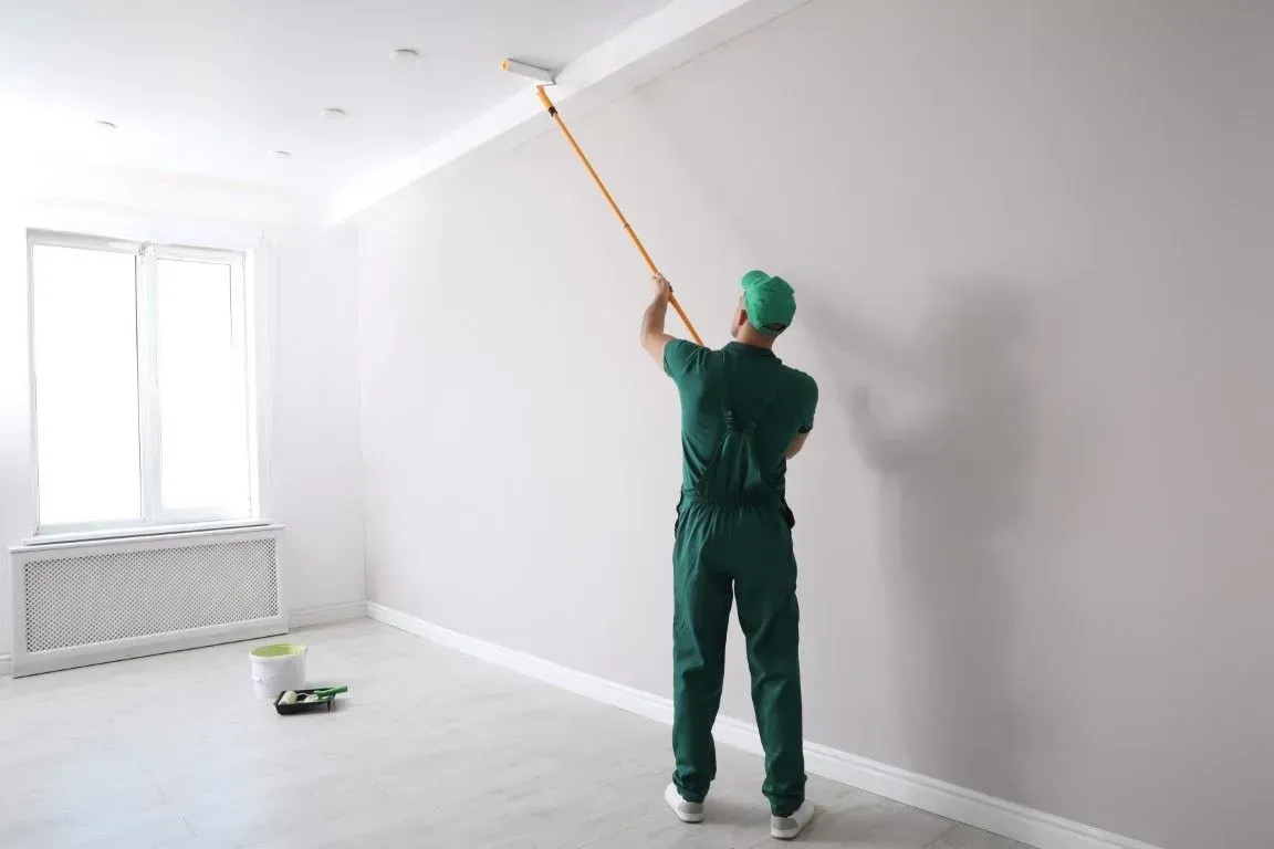 Person painting a white wall with a long roller in an empty room