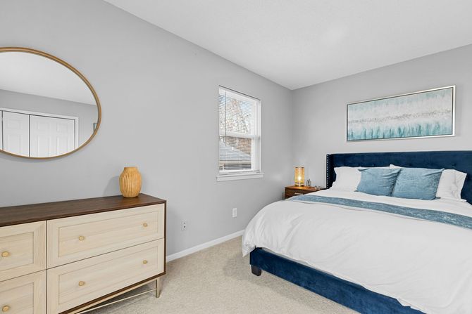 Bright bedroom with light gray walls, blue bedding, dresser, mirror, and coastal wall art