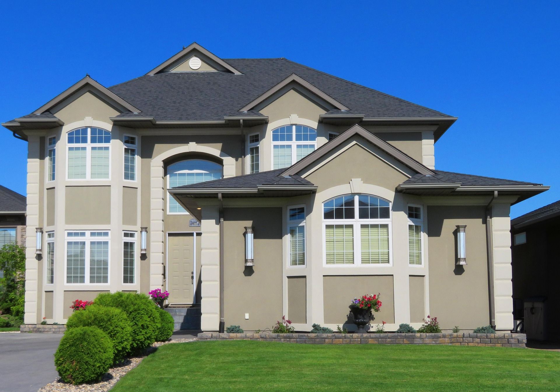 Large beige two-story suburban house with gray roof, white trim, and manicured green lawn