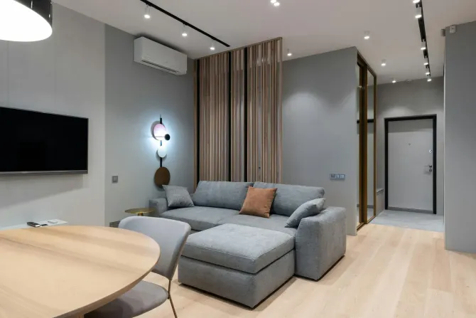 Modern living room with gray sectional sofa, wood accents, wall TV, and hallway view