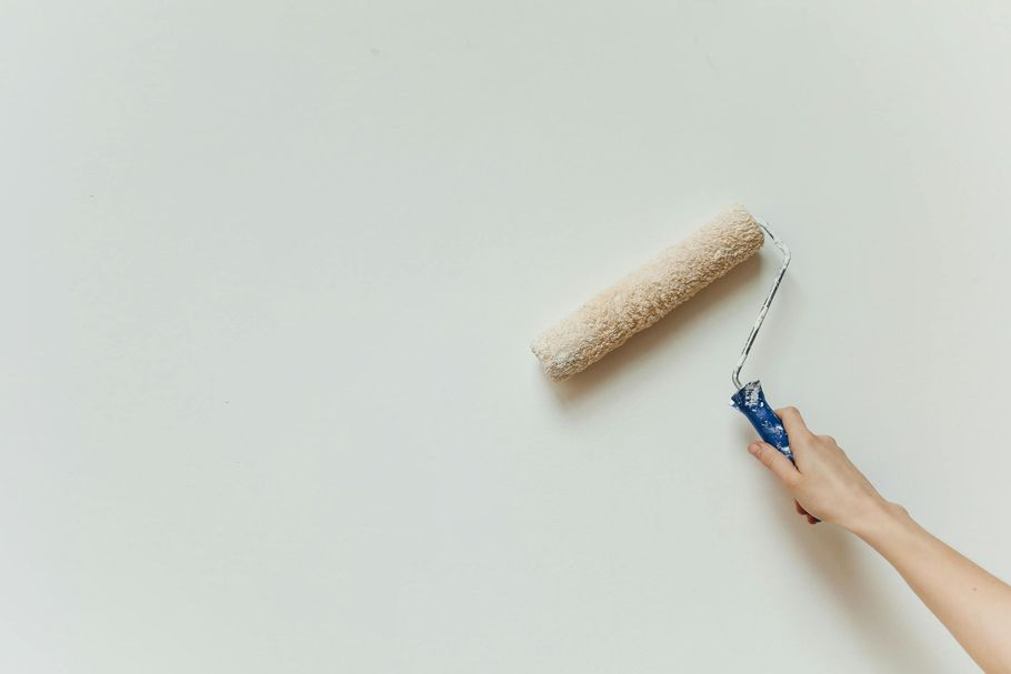Hand rolling a beige paint roller on a white wall with blue handle