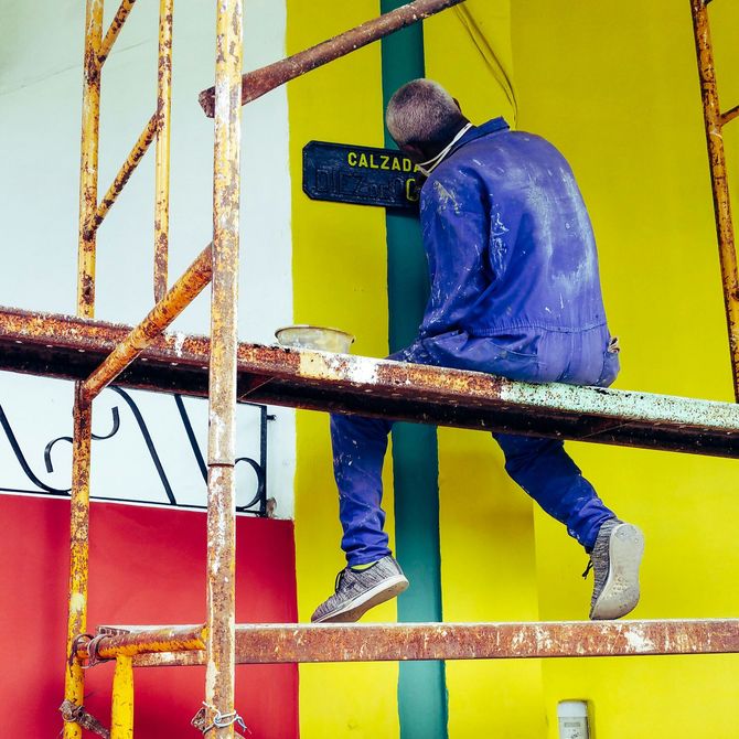 Worker in blue paint-splattered clothes painting a colorful wall from scaffolding
