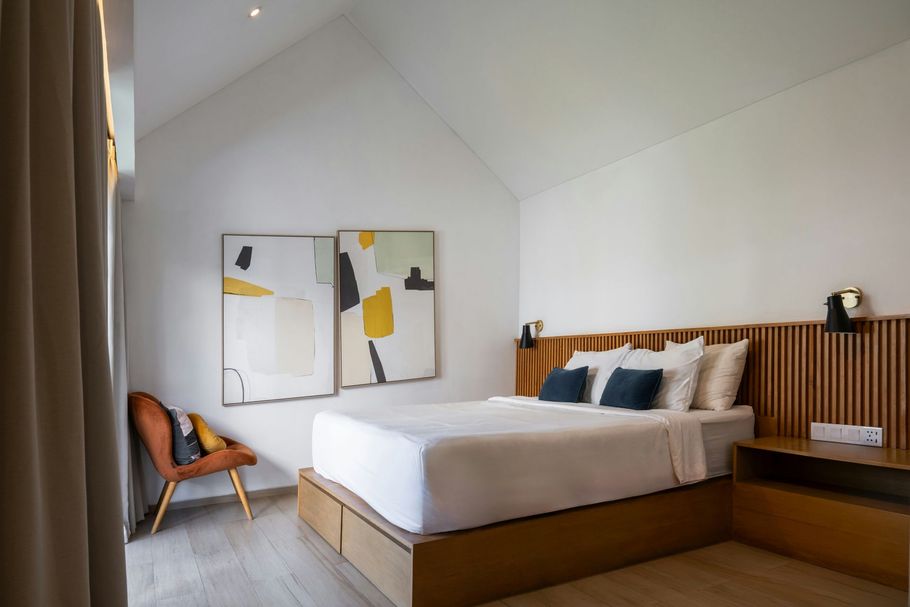 Modern bedroom with a wooden bed, abstract wall art, and a chair by the window