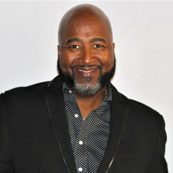 A bald man with a beard wearing a black jacket and polka dot shirt