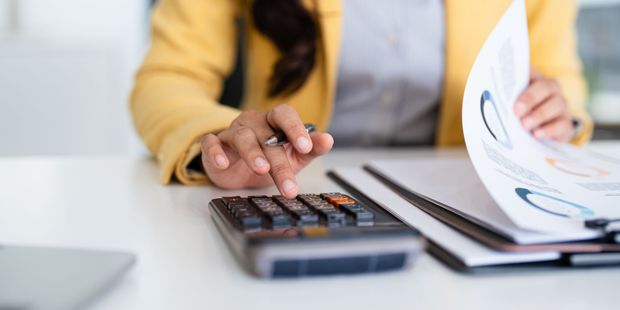Person in yellow blazer using calculator and reviewing papers with charts. Person in yellow blazer using calculator and reviewing papers with charts.