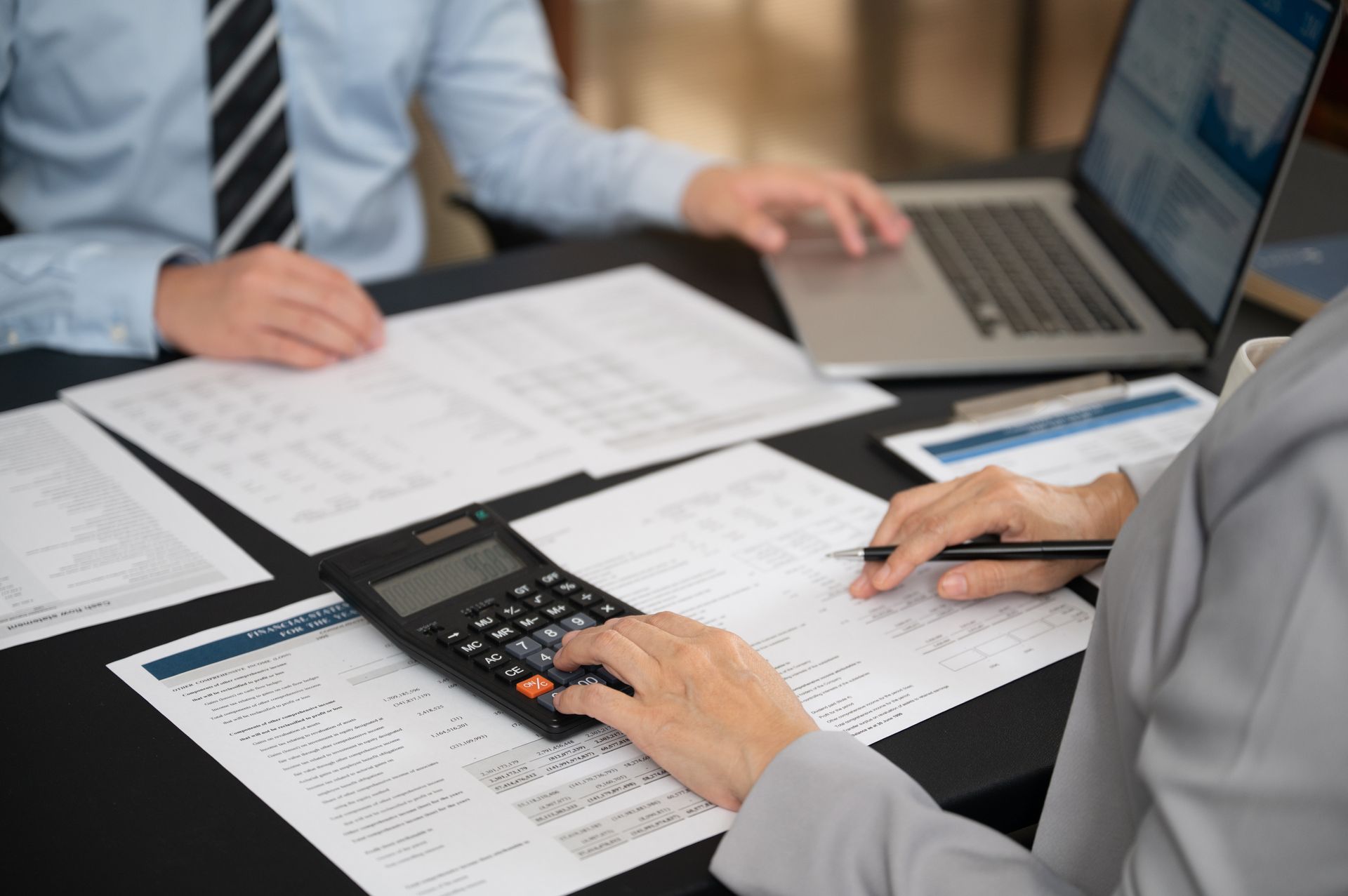 Two people reviewing financial documents, using a calculator and laptop.