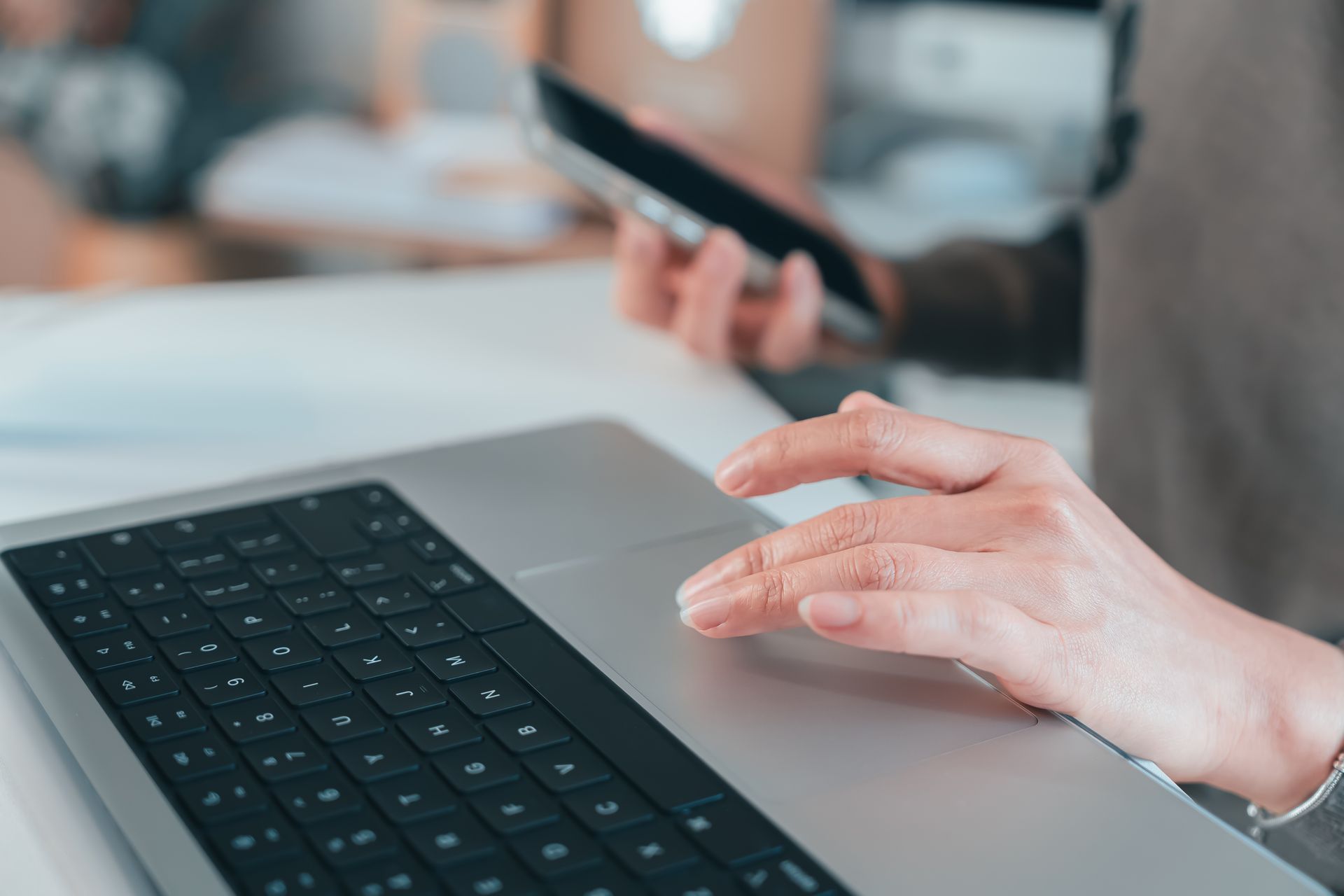Person using laptop, operating trackpad with one hand and holding a smartphone with the other.