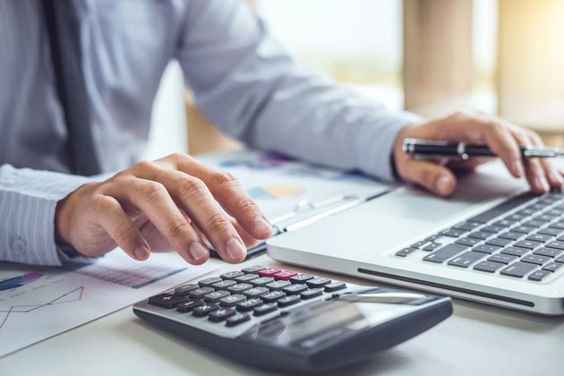 Person's hands using a calculator and laptop, working on financial documents at a desk. Person's hands using a calculator and laptop, working on financial documents at a desk.