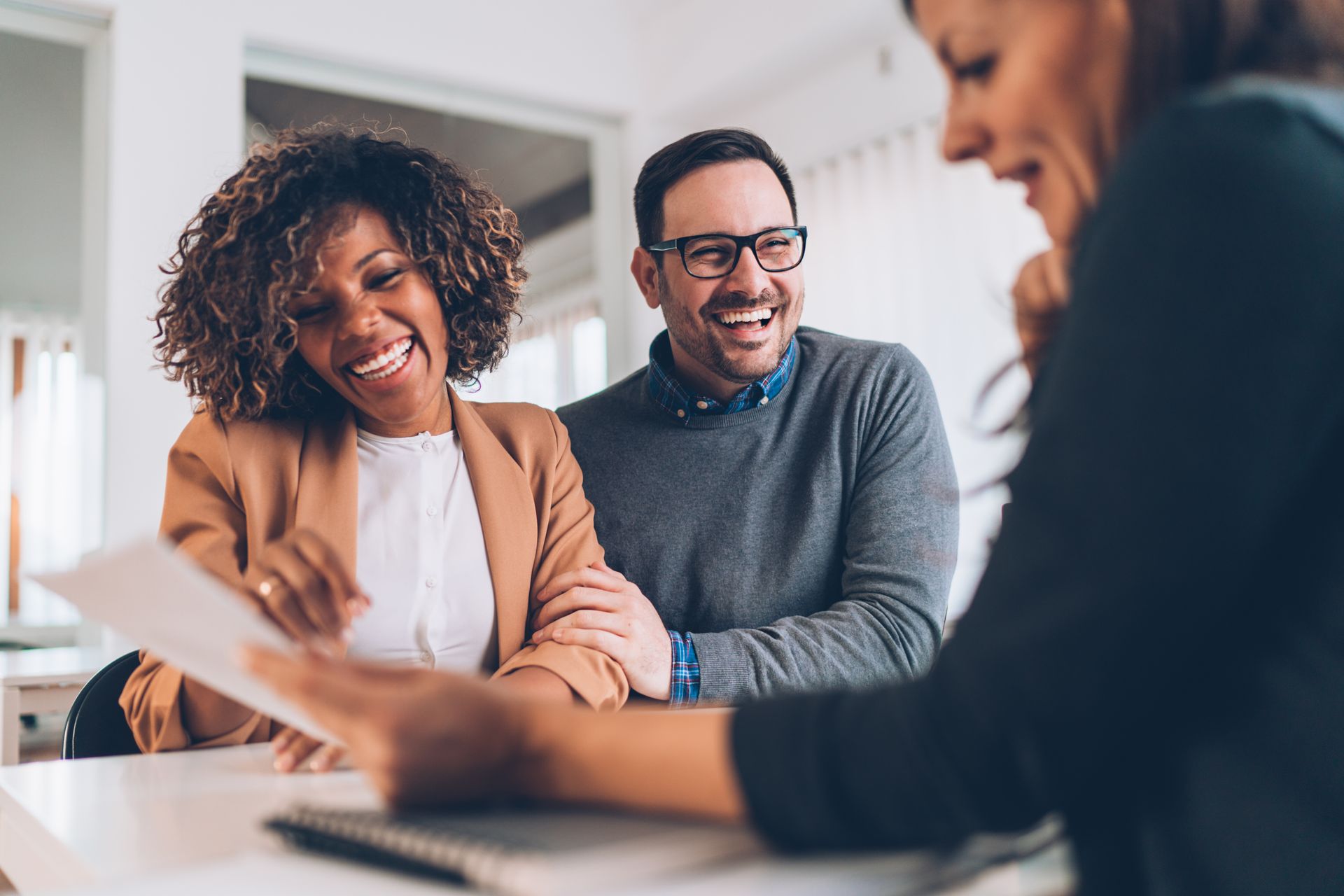 Couple laughing, reviewing documents with a person in an office setting.