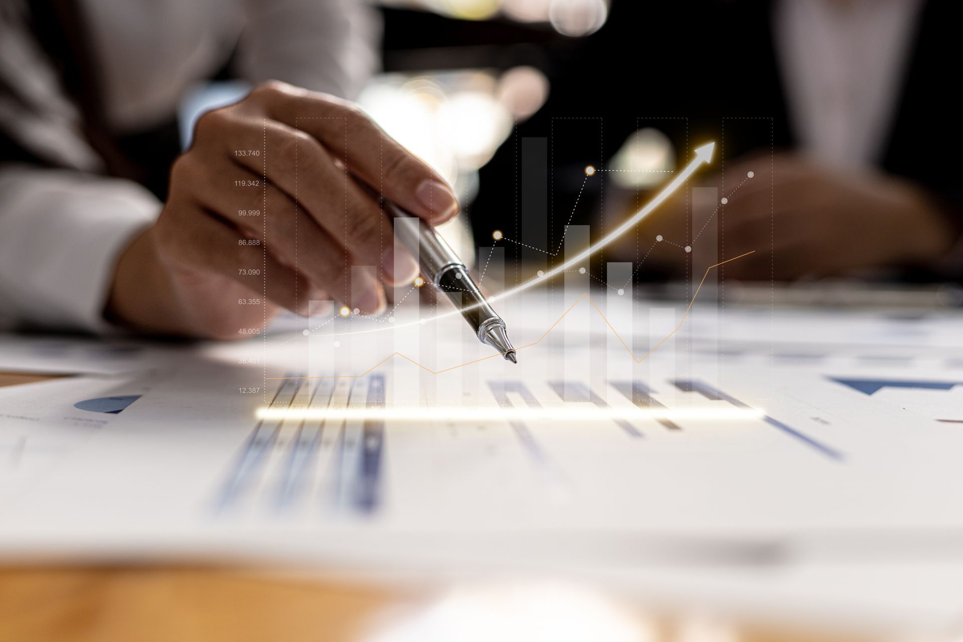 Hand with pen pointing to a financial chart with an upward trend overlaid on documents.