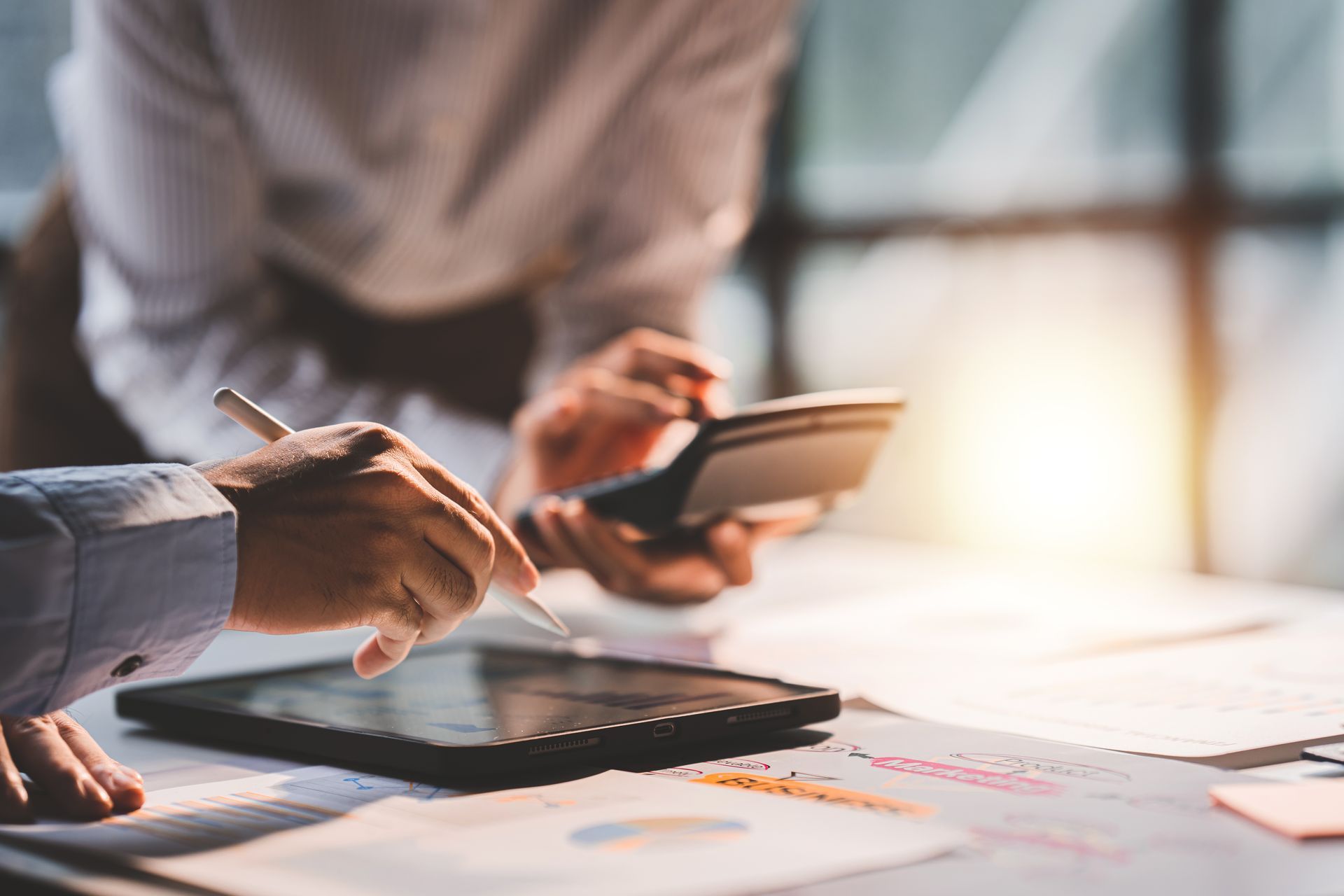 Two people working together on financial documents, using a calculator and tablet.