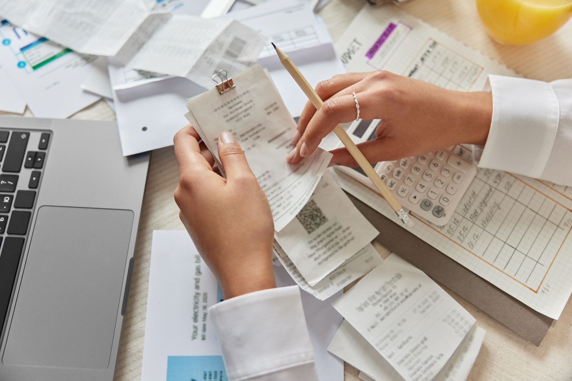 Hands sorting receipts at a desk with a laptop, calculator, and papers.