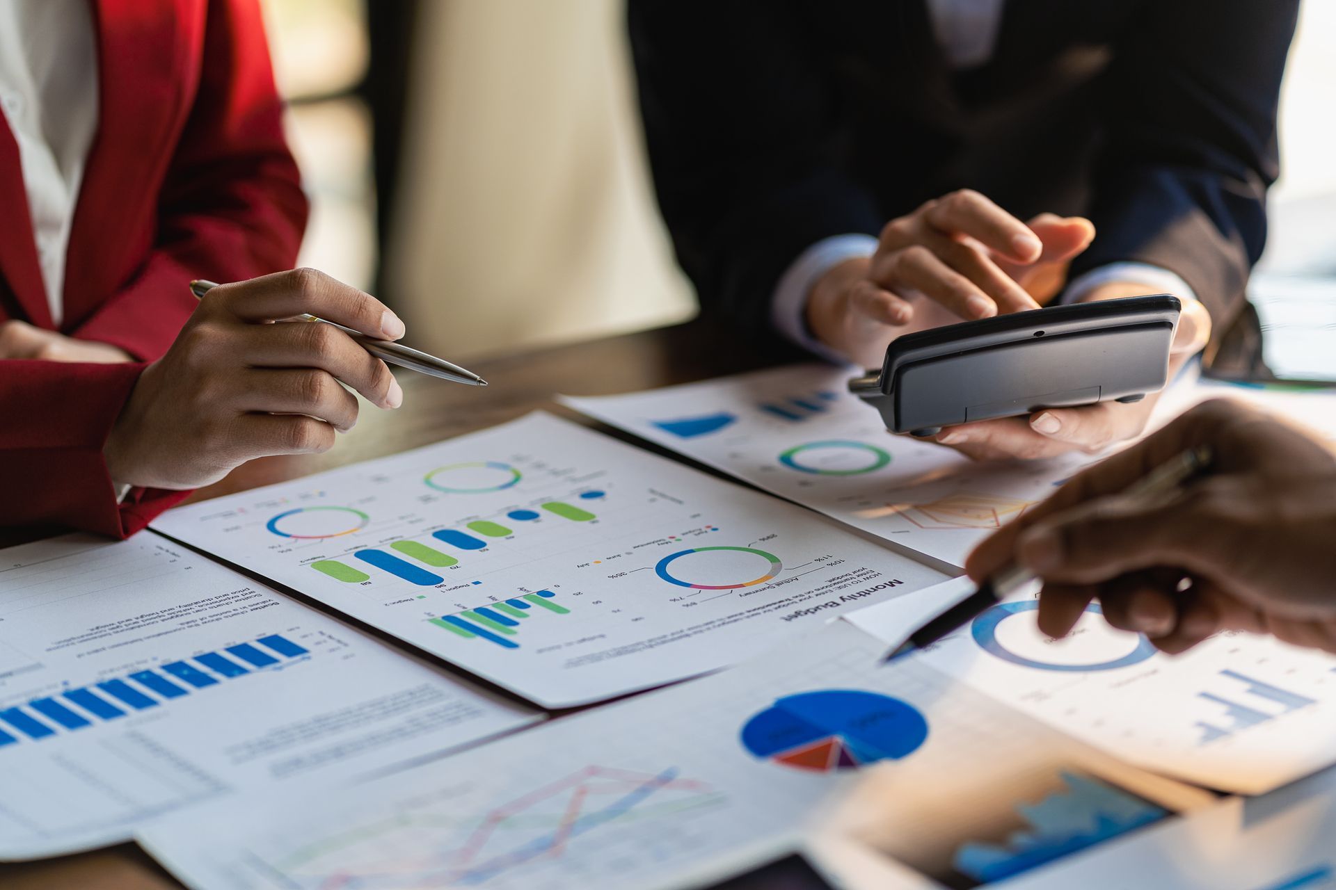 People reviewing financial charts and using a calculator at a table. People reviewing financial charts and using a calculator at a table.