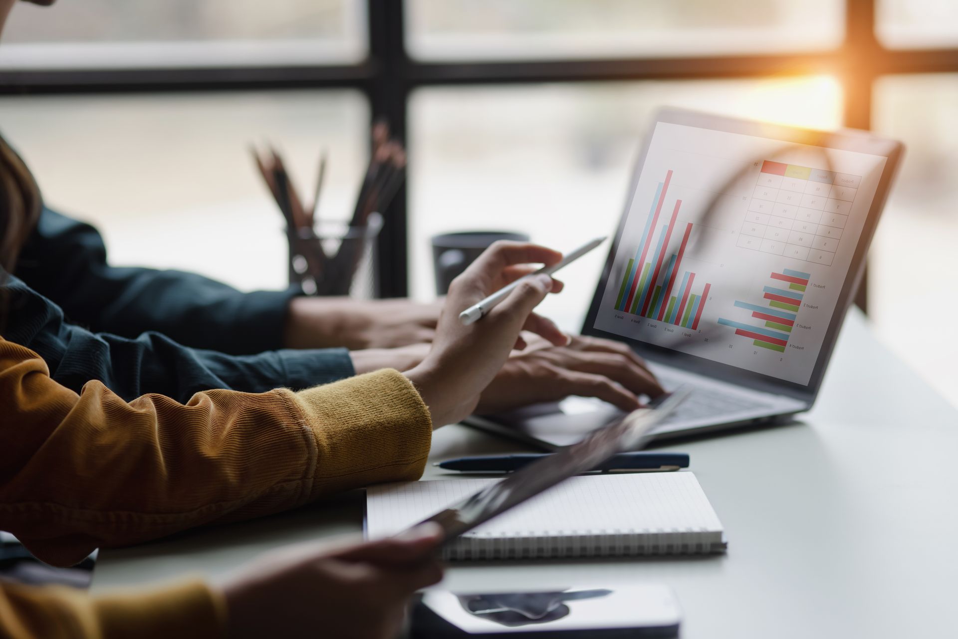 Two people collaborating, reviewing graphs on a laptop screen, hands pointing. Two people collaborating, reviewing graphs on a laptop screen, hands pointing.