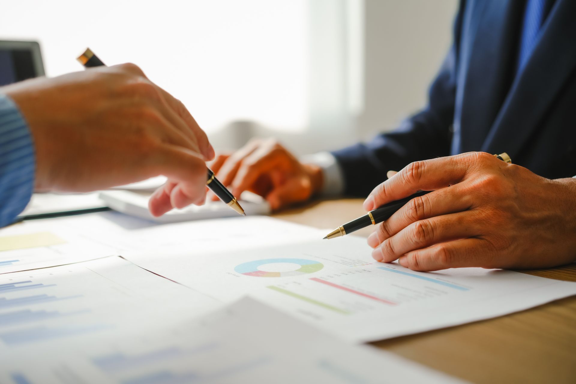 Two people in suits analyzing financial documents with pens. Two people in suits analyzing financial documents with pens.