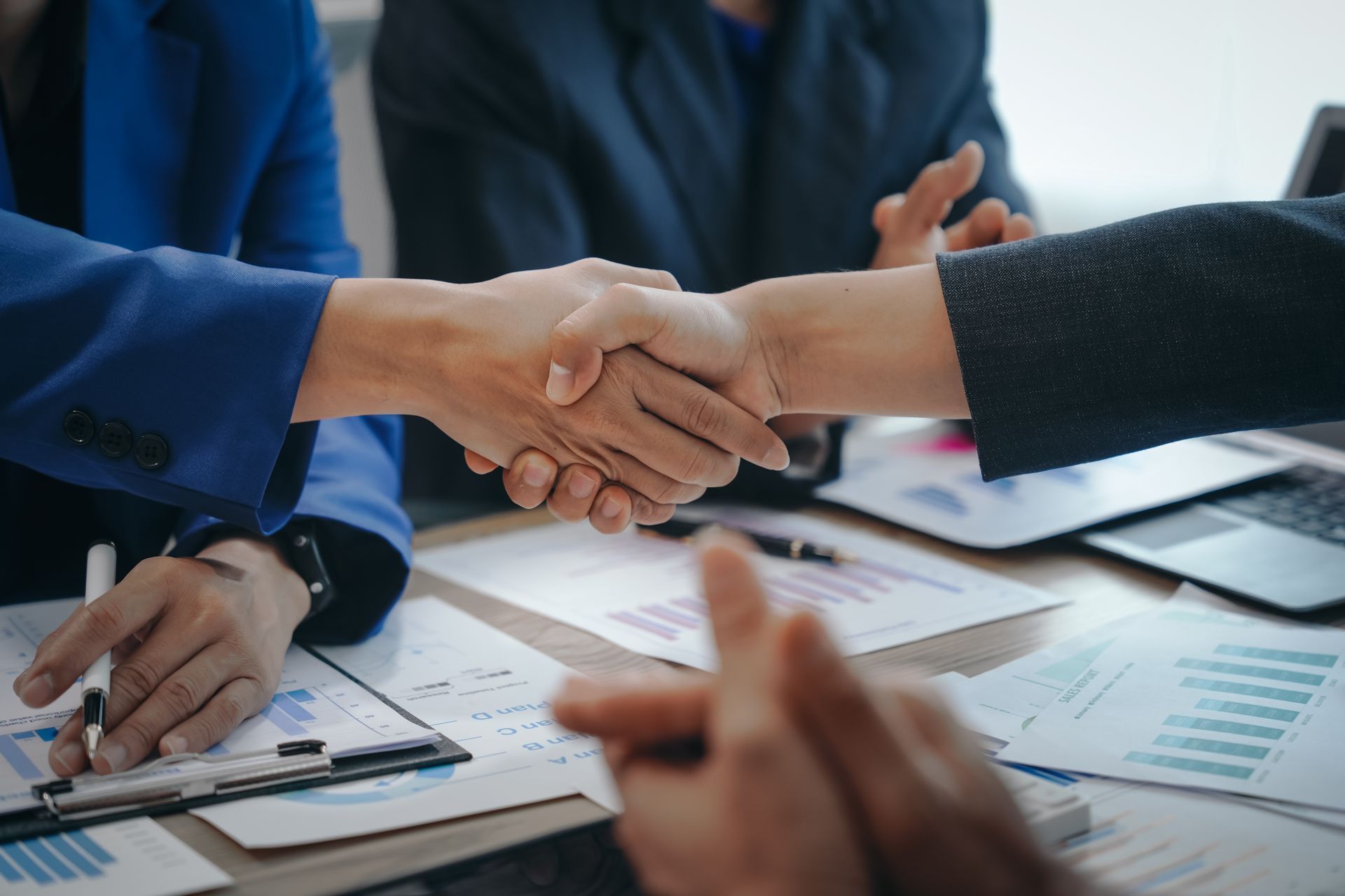 People shaking hands over a table with papers, celebrating a business agreement.