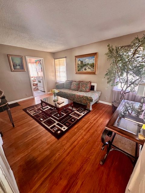 Living room with wooden floors, sofa, coffee table, rug, artwork, and an open doorway.