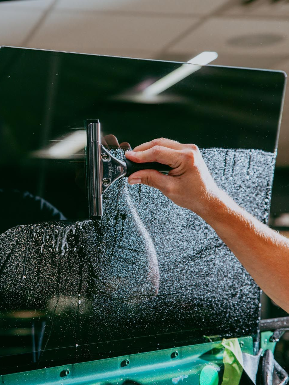 Person applying window tint with a tool and heat gun on a white surface.