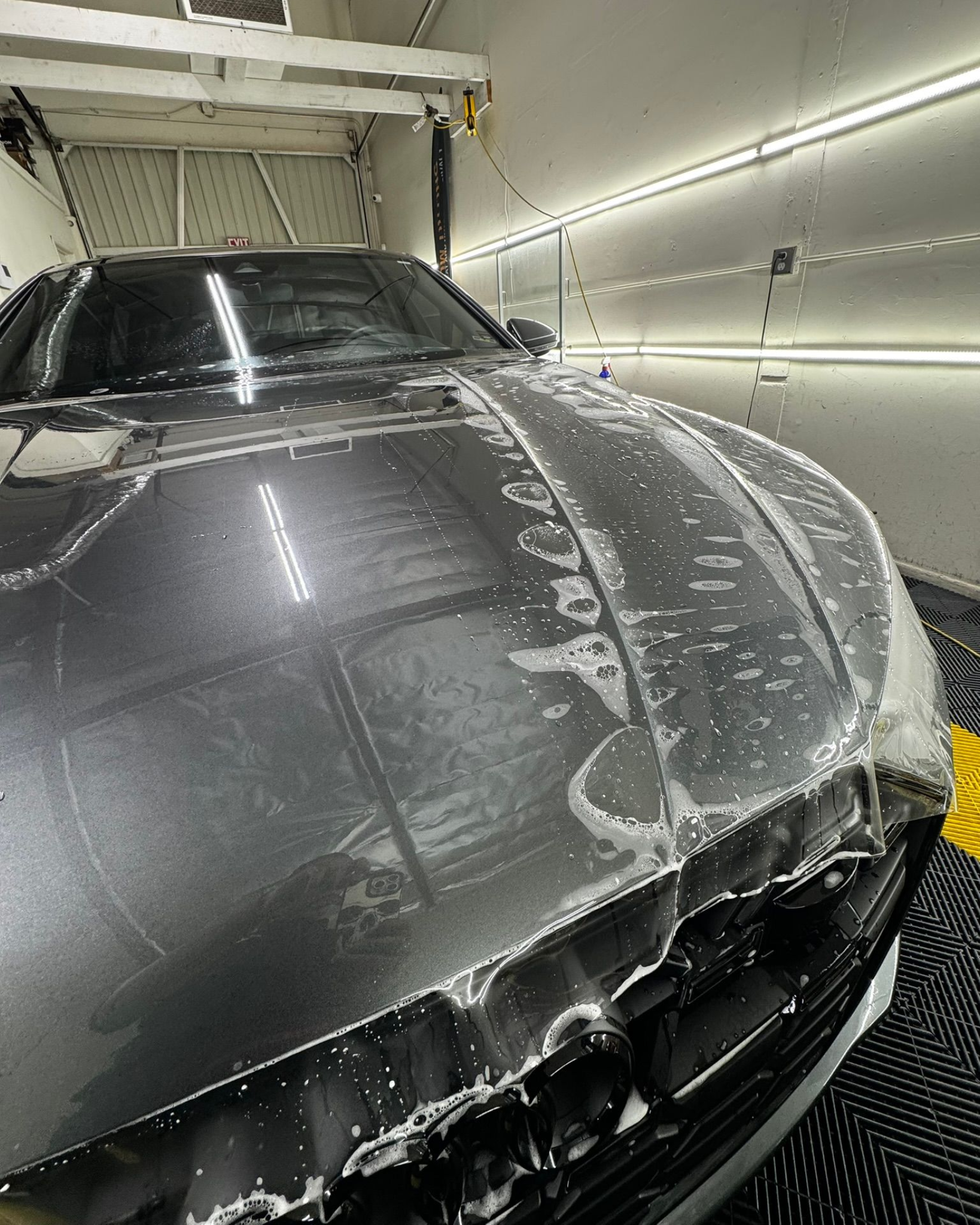 Car being worked on in a shop, with protective film applied to the front.