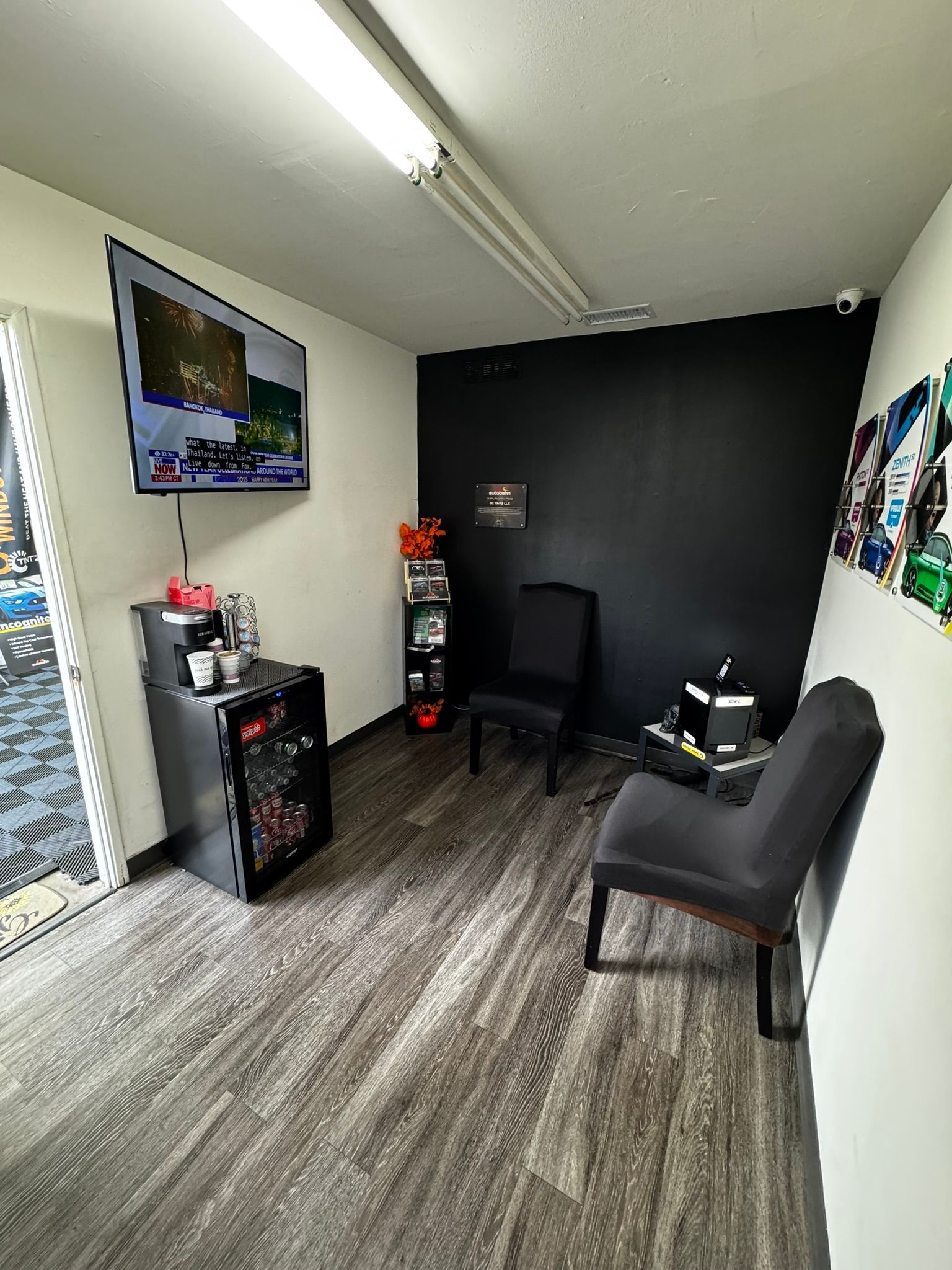 Waiting room with TV, chairs, black wall, and drinks.