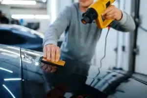 Person applying film to a car, using a heat gun and squeegee.