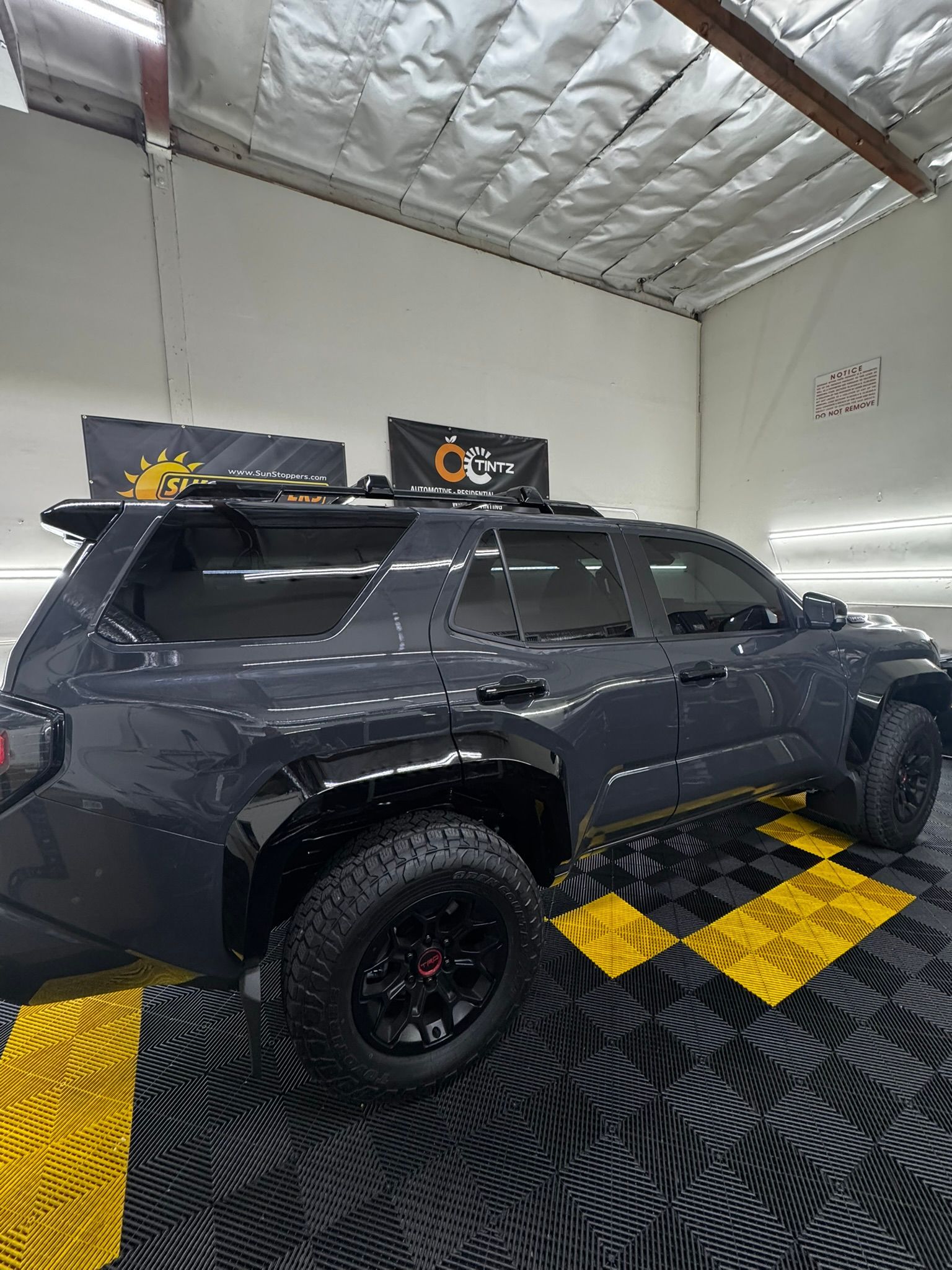 Dark gray SUV with black wheels and roof rack on black and yellow checkered floor.