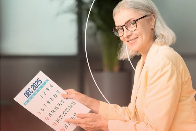 Smiling woman holding a December 2025 calendar in a bright indoor setting