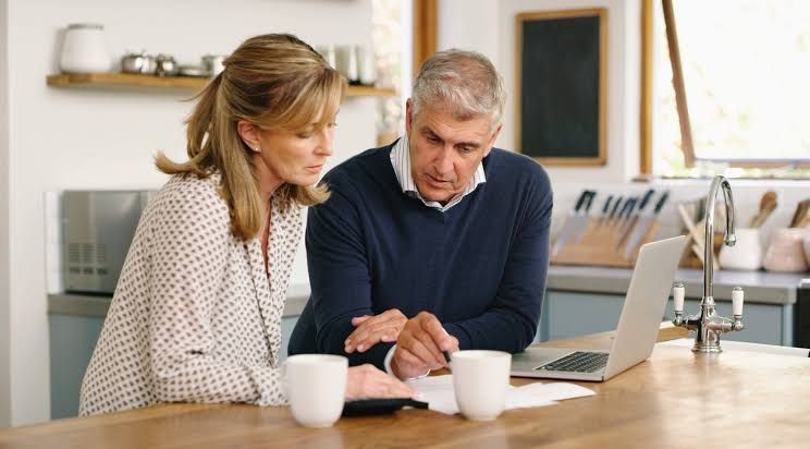 Two coworkers reviewing a laptop together at a kitchen table with coffee mugs.