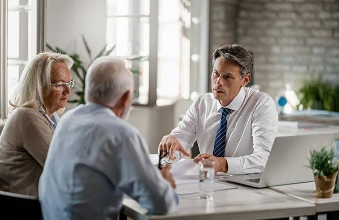 Three people in a meeting at a table, discussing documents in a bright office