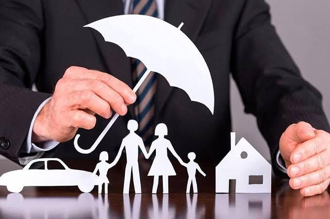 Businessman shielding paper family, house, and car with an umbrella