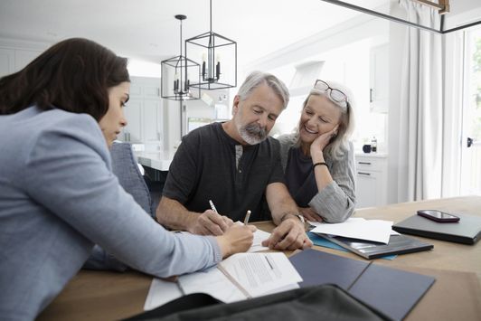 Three people discussing documents at a conference table in a bright office.