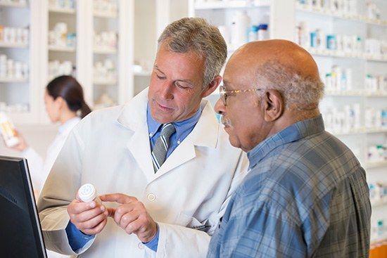 Pharmacist showing an elderly customer a pill bottle at a pharmacy counter