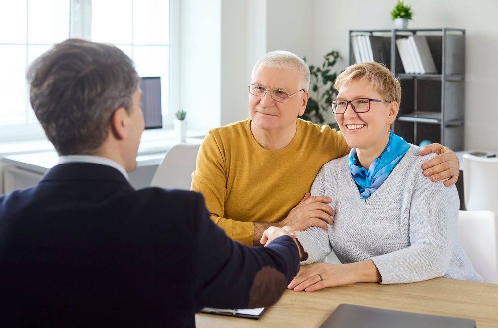 Two people smile at a man shaking hands across a desk in a bright office