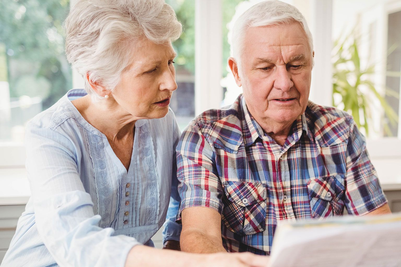 Older couple reading a newspaper together at a table in a bright room