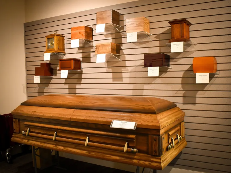 A wooden coffin is sitting in front of a wall of wooden urns.