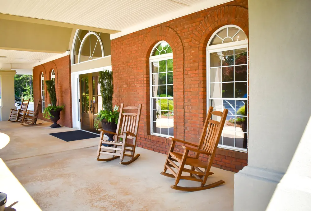 Two rocking chairs are on a porch in front of a brick building