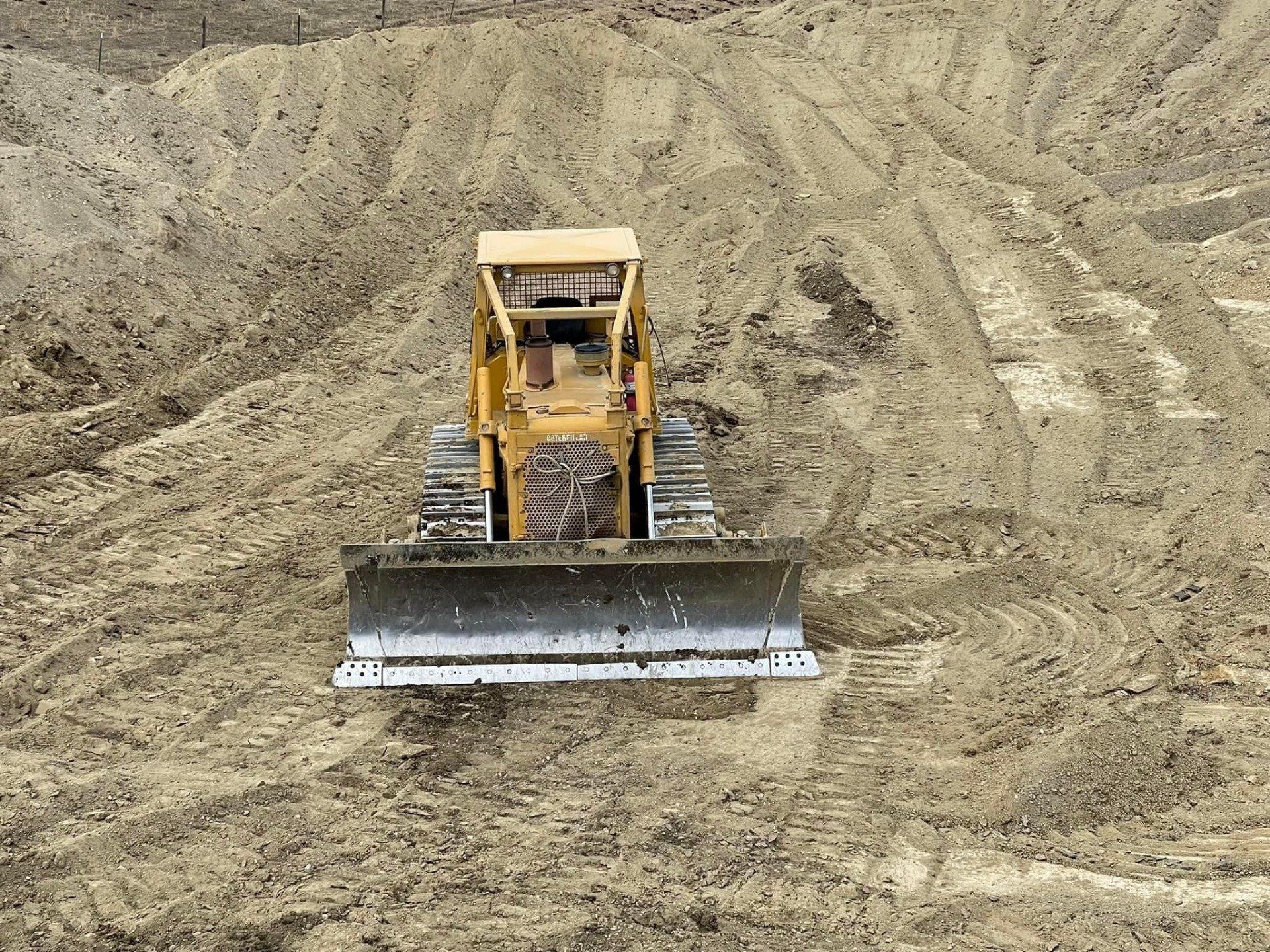 Yellow bulldozer on dirt terrain, with blade down. Tracks visible.