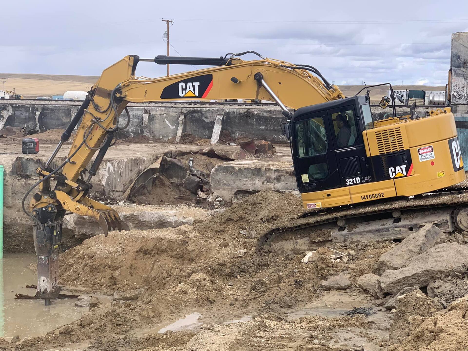 Yellow excavator demolishing concrete structure at a construction site.