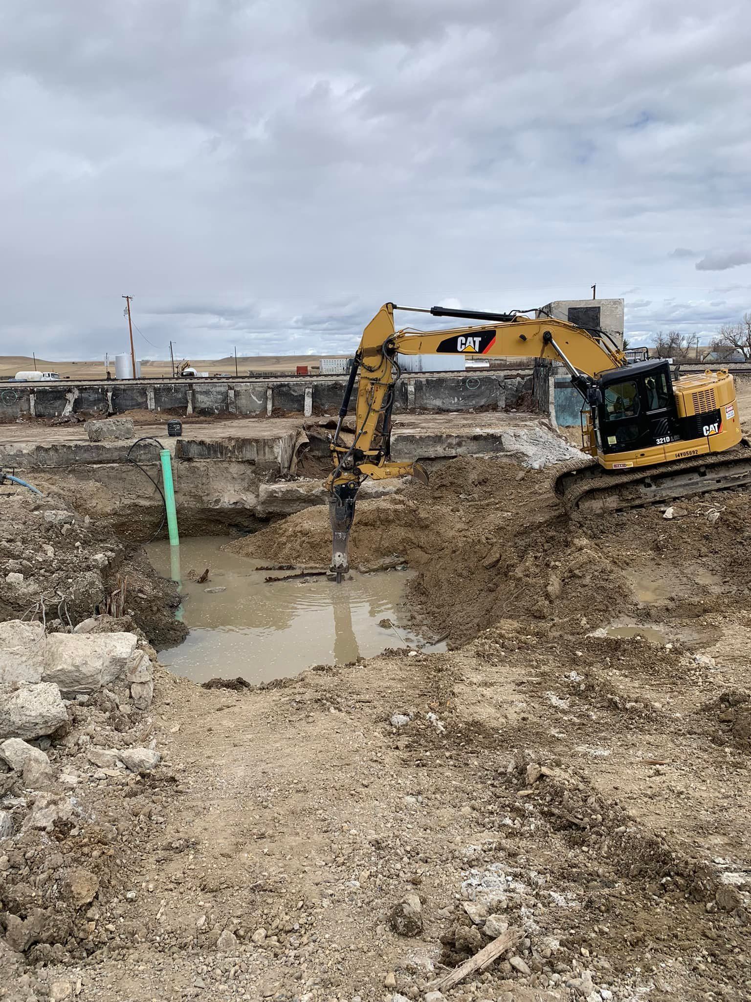Excavator digging in muddy construction site. Cloudy sky.