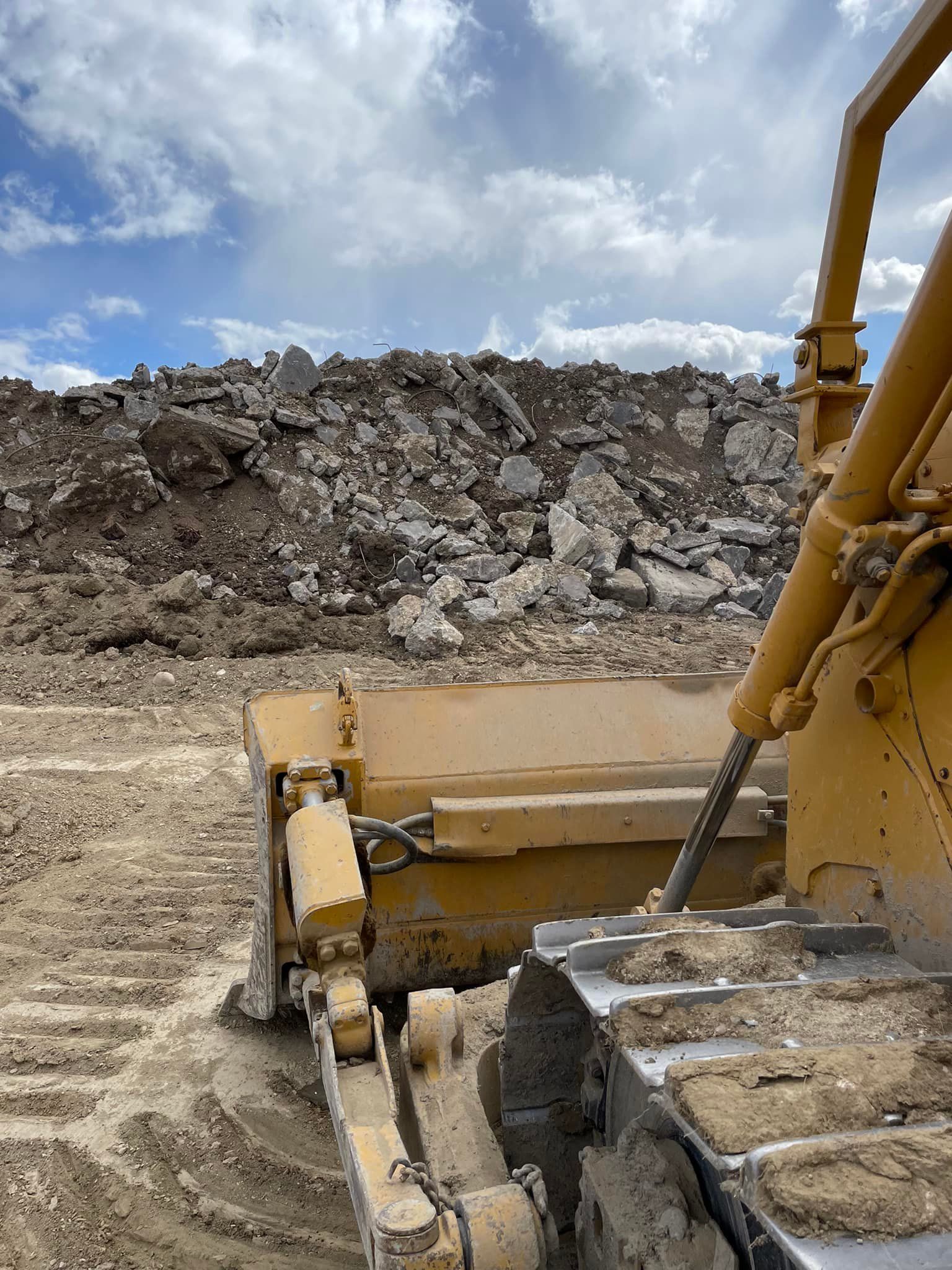 Yellow bulldozer pushing debris, construction site, cloudy sky.