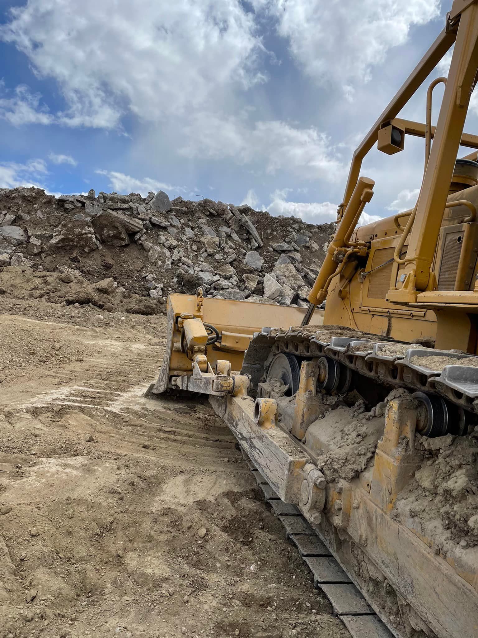 Yellow bulldozer pushing earth at a construction site, blue sky in background.