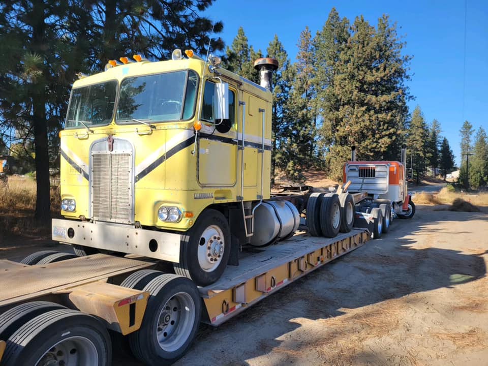 Yellow Kenworth semi-truck on a flatbed trailer, in a rural setting.