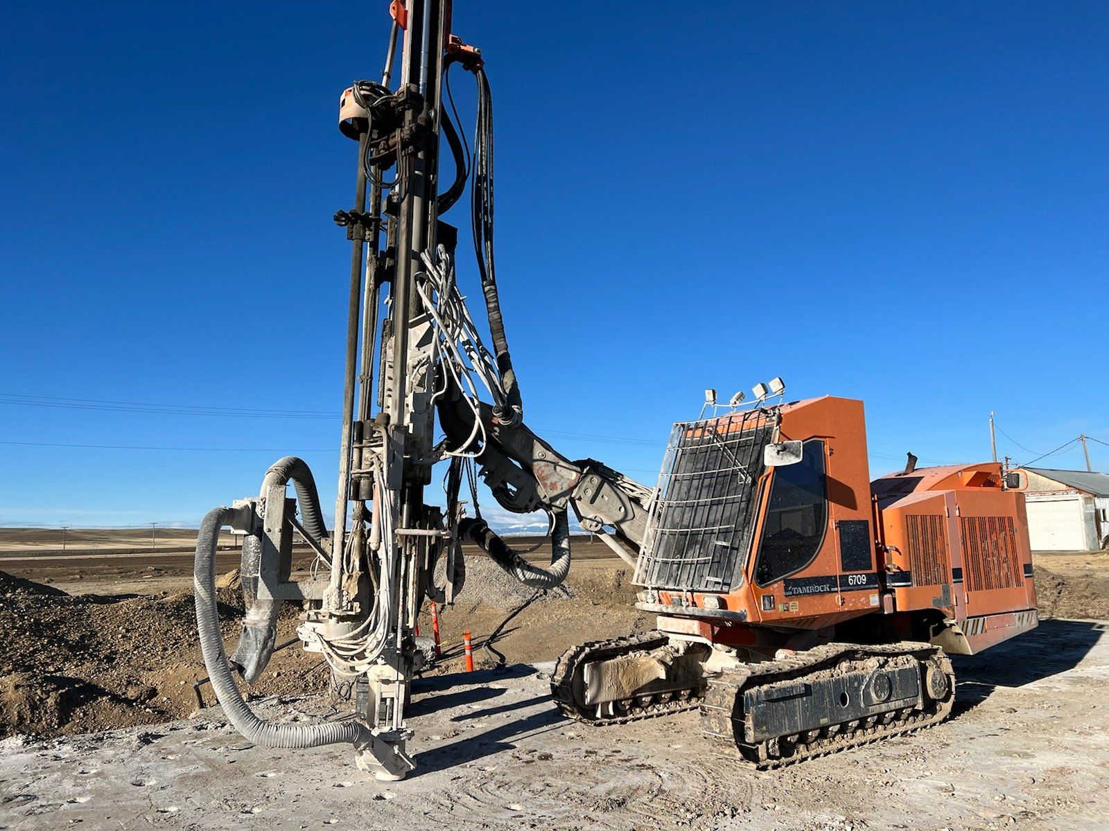 Orange drill rig on tracks against a clear blue sky, likely for construction.