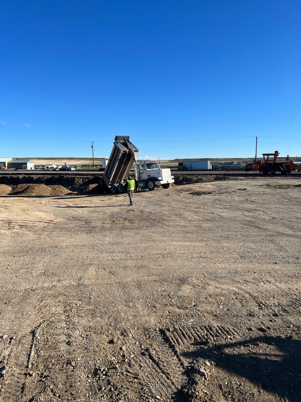 Dump truck dumping soil on a construction site; worker nearby. Blue sky.