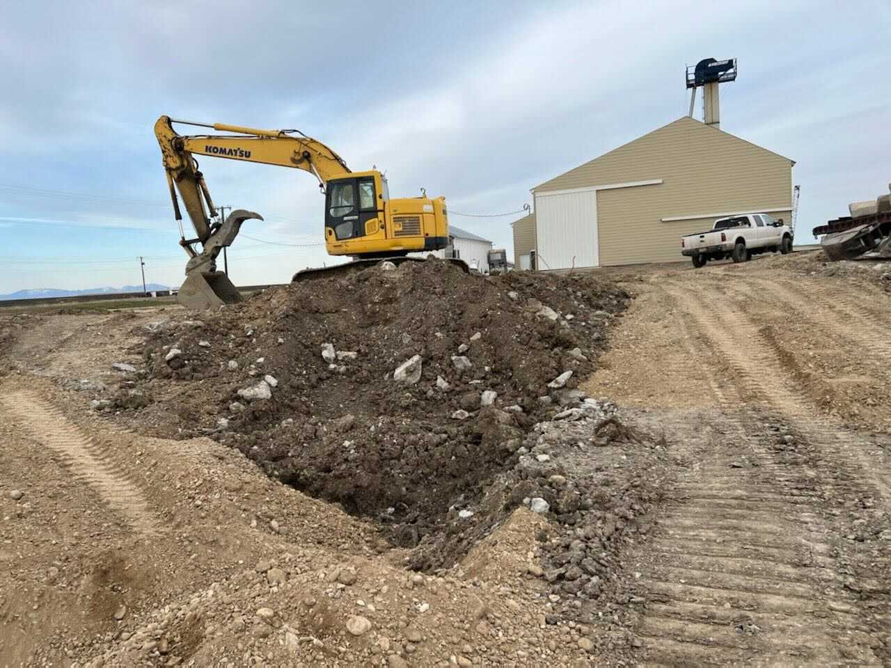 Yellow excavator digging earth on a construction site; building in the background.