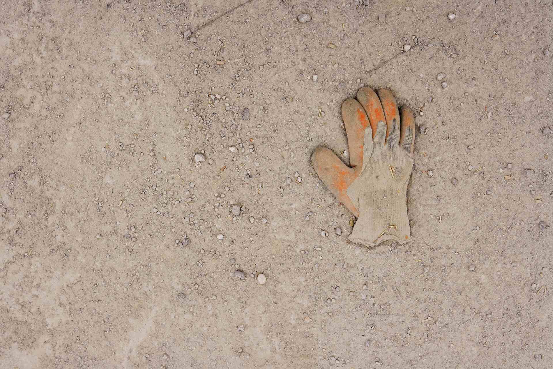 Work glove, orange and beige, lying on sandy ground.